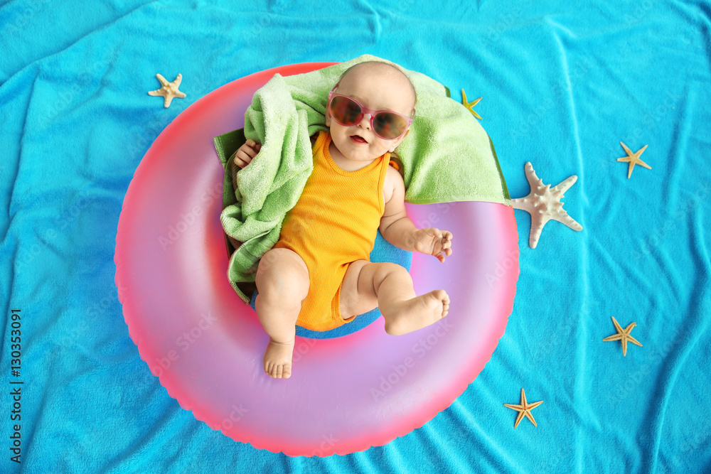 Cute baby with swimming ring, towel and sunglasses lying on blue bedspread. Holidays at sea with baby, concept Cute baby with swimming ring, towel and sunglasses lying on blue bedspread. Holidays at sea with baby, concept
