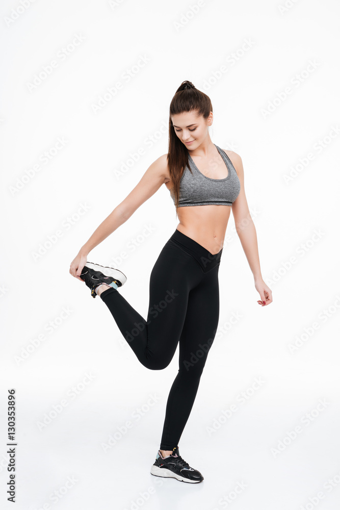 Portrait of a smiling sports woman standing and stretching leg