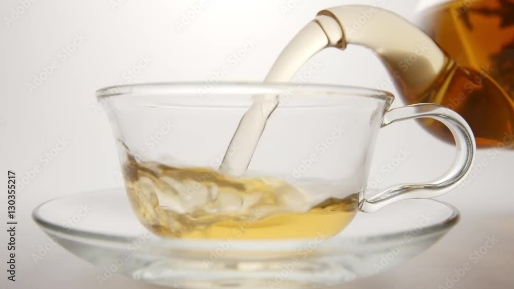 SLOW MOTION: Fresh tea flows in a tea cup from a teapot SLOW MOTION: Fresh tea flows in a tea cup from a teapot