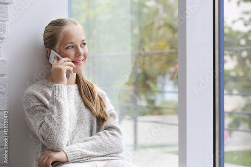 Happy teenager talking on phone near window