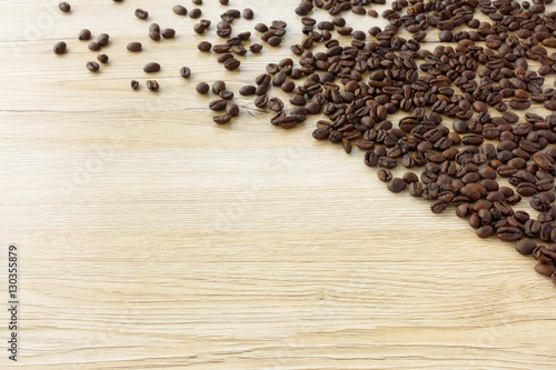 Fresh roasted coffee beans spread out towards the light on brown wooden background with lots of copy space.