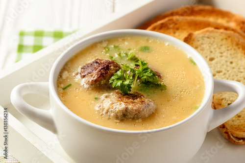 Vegetable cream soup with meatballs on white wooden background.