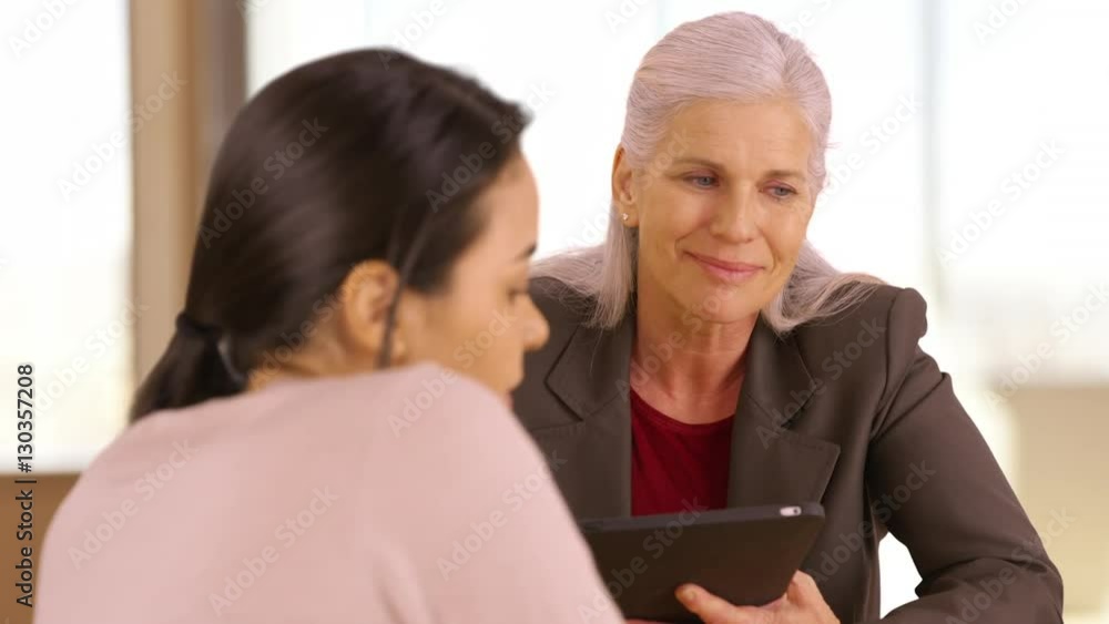 A smiling business executive has a meeting with her employee. An older office worker with a tablet meets with an employee. A smiling business executive has a meeting with her employee. An older office worker with a tablet meets with an employee.