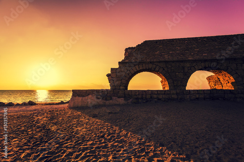 Remains of the ancient Roman aqueduct in ancient city Caesarea at sunset. Israel. photo