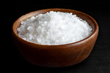 Coarse salt in wooden dish isolated on black.