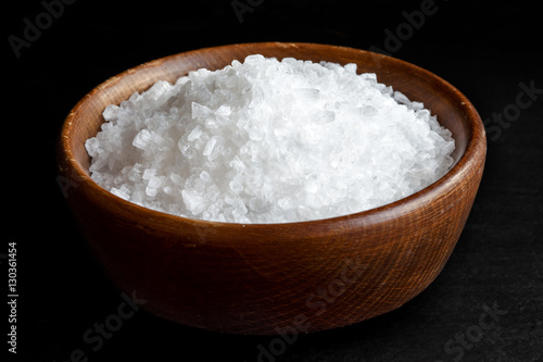 Coarse salt in wooden dish isolated on black.