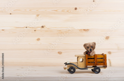 Wooden truck carries a teddy bear. Pine wood background as a backdrop