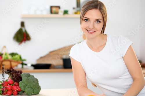 Young woman is ready for cooking in a kitchen. Housewife sitting at the table and looking at the camera