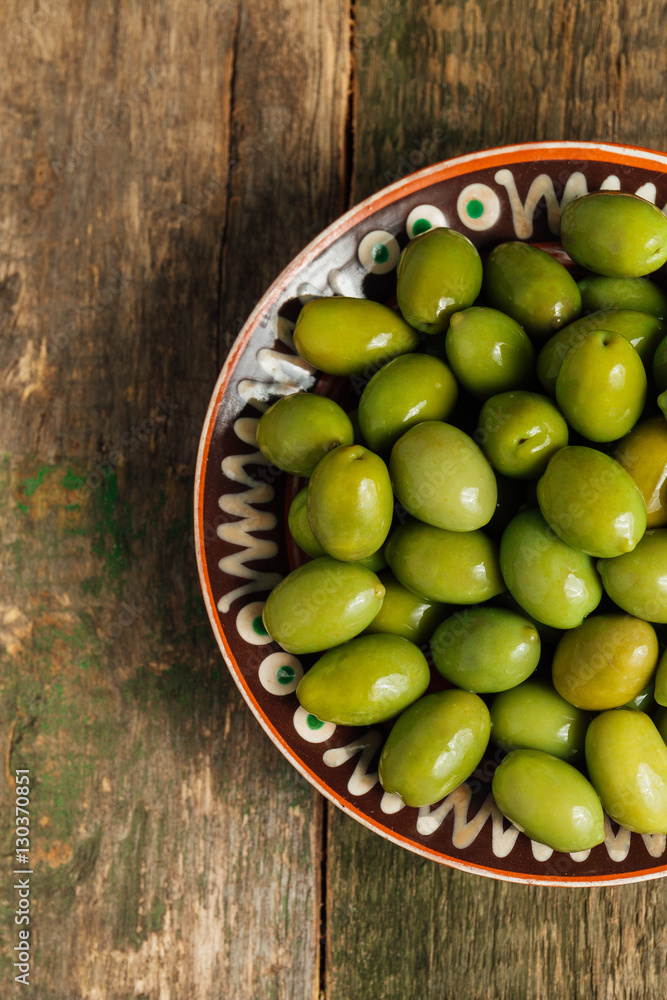 Green olives in brown bowl on wooden background. Top view. Copy space. Green olives in brown bowl on wooden background. Top view. Copy space.
