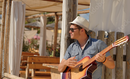 young  man wearing straw hat playing guitar on the beah