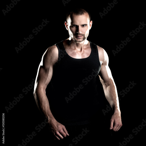 muscular man, clasps hands in fist, black background, place for text on the right