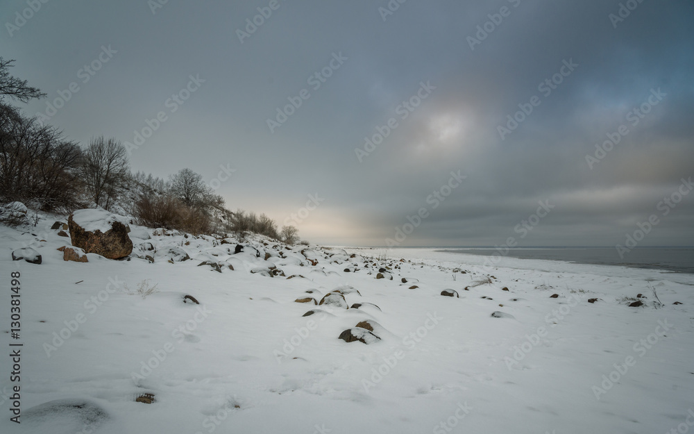 snowy rocky shore of the lake on background gray cloudy sky