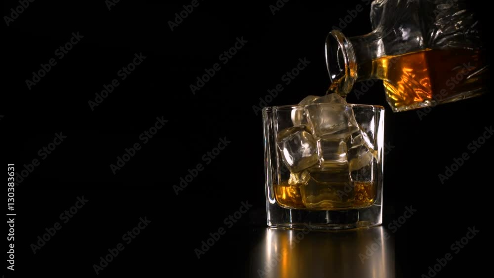 Whiskey on the rocks poured from a rystal decanter on black backround copy space Whiskey on the rocks poured from a rystal decanter on black backround copy space