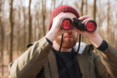 Concentrated bearded man wearing hat looking at field-glass