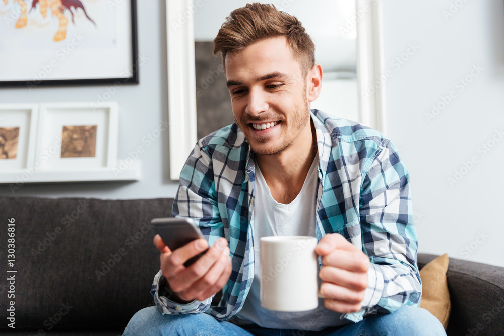Cheerful young bristle man holding cup of tea while chatting. Cheerful young bristle man holding cup of tea while chatting.
