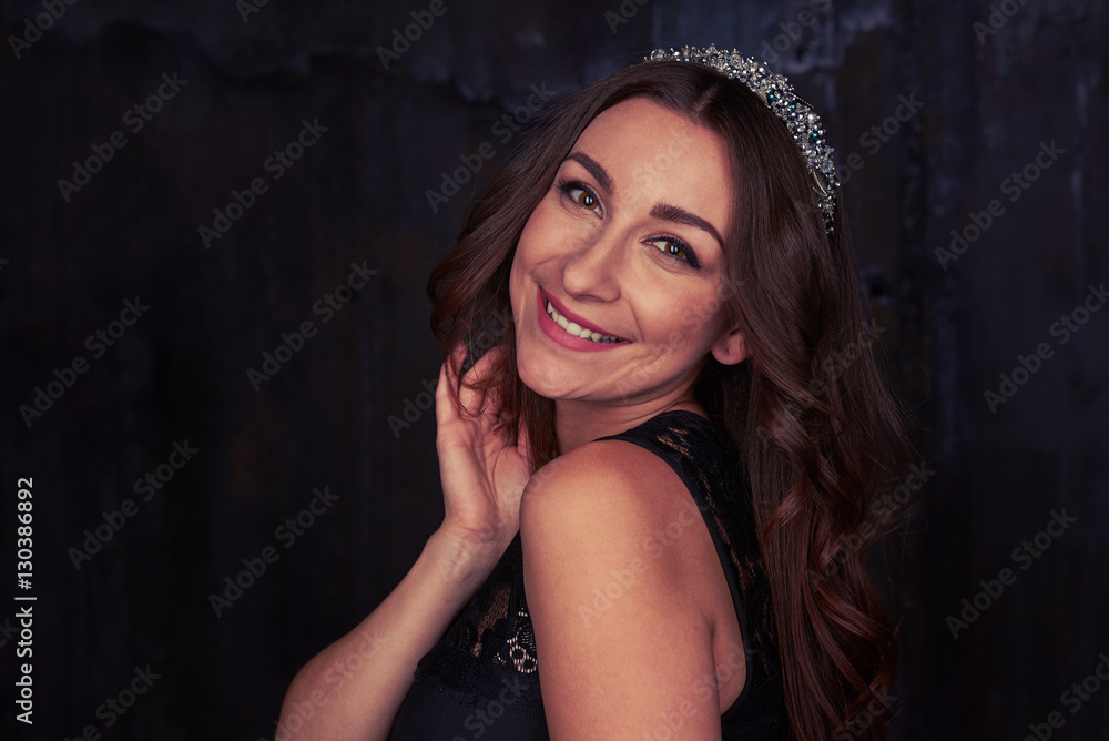 Elegant woman with curly hair and a diadem smiling over her shou