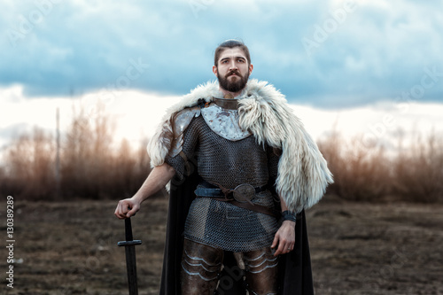 Vászonkép Formidable man warrior in armor and sword standing in a field and protects