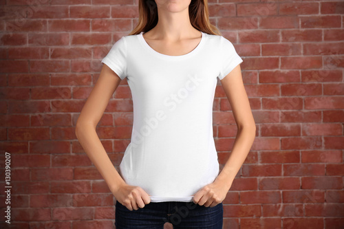 Young woman in blank white t-shirt standing against brick wall, close up