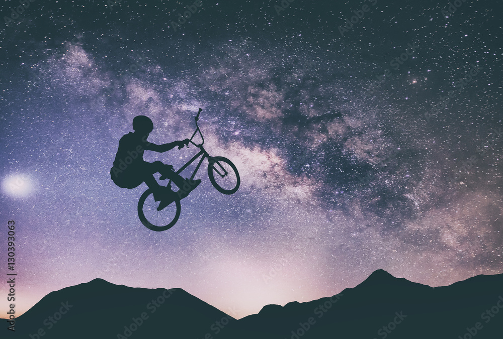 Man riding a bike performing a trick against on Mountain with Milky way.