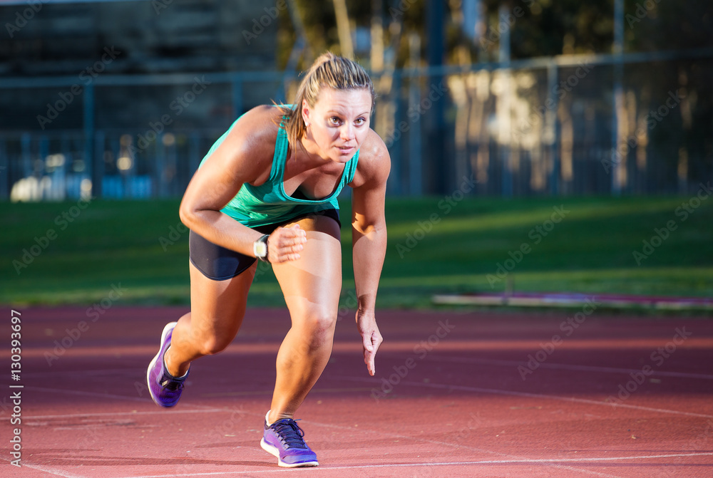 Female fitness athlete setting of on a race on a tartan athletics track
