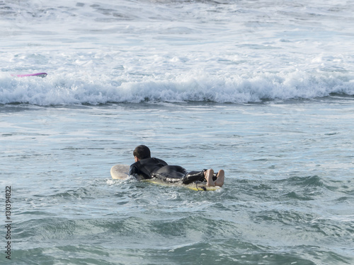 Fotografija Single male surfer lying on his board paddling out the surf to c