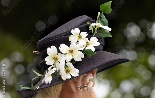 Race-goer wearing a hat with flowers in typical Ascot fashion at Royal Ascot Races. She is taking a call on her mobile cell phone. photo