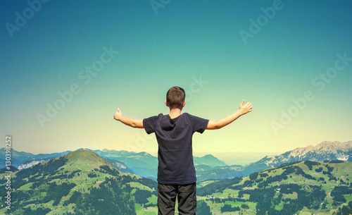 Young boy with hands up standing on the peak of the mountain