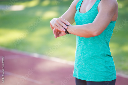 Fit female athlete looking at her heart rate monitor during a training session on a tartan athletic track