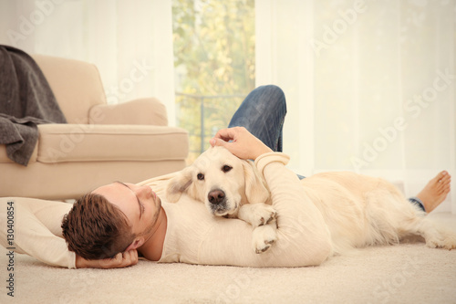 Handsome man with dog lying on carpet at modern room interior