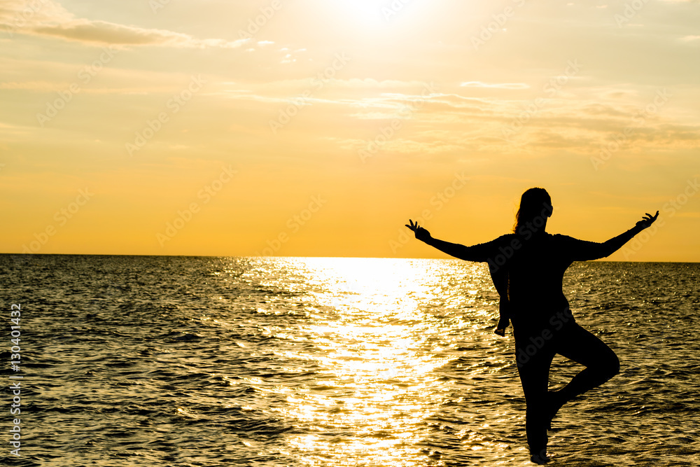 Female yoga vriksasana silhouette on beautiful beach during sunset.