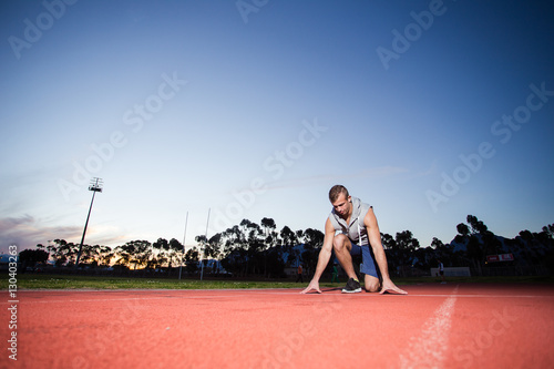 Male sprinter athlete on a tartan athletic track getting ready f © Dewald