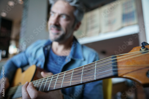 Mature trendy guy playing the guitar in a bar