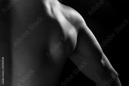 Male fitness model showing muscles in studio with a black backgr