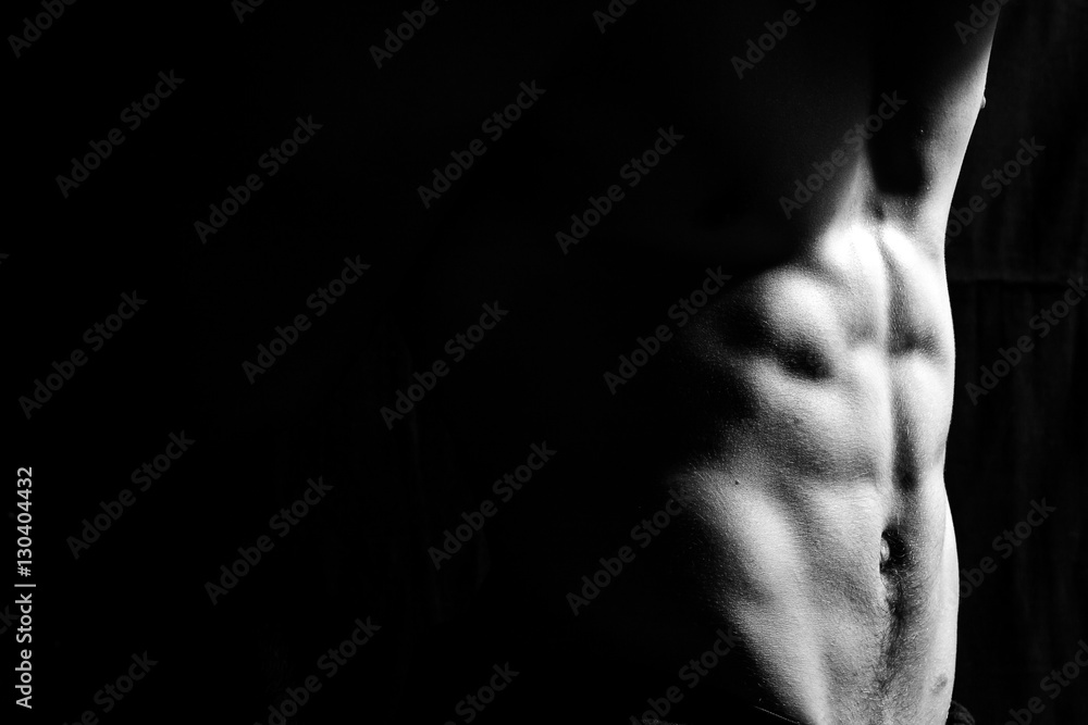 Male fitness model showing muscles in studio with a black backgr Male fitness model showing muscles in studio with a black backgr