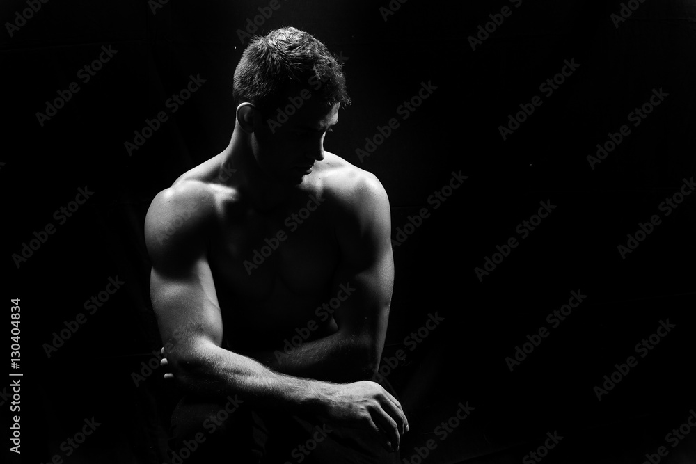 Male fitness model showing muscles in studio with a black backgr