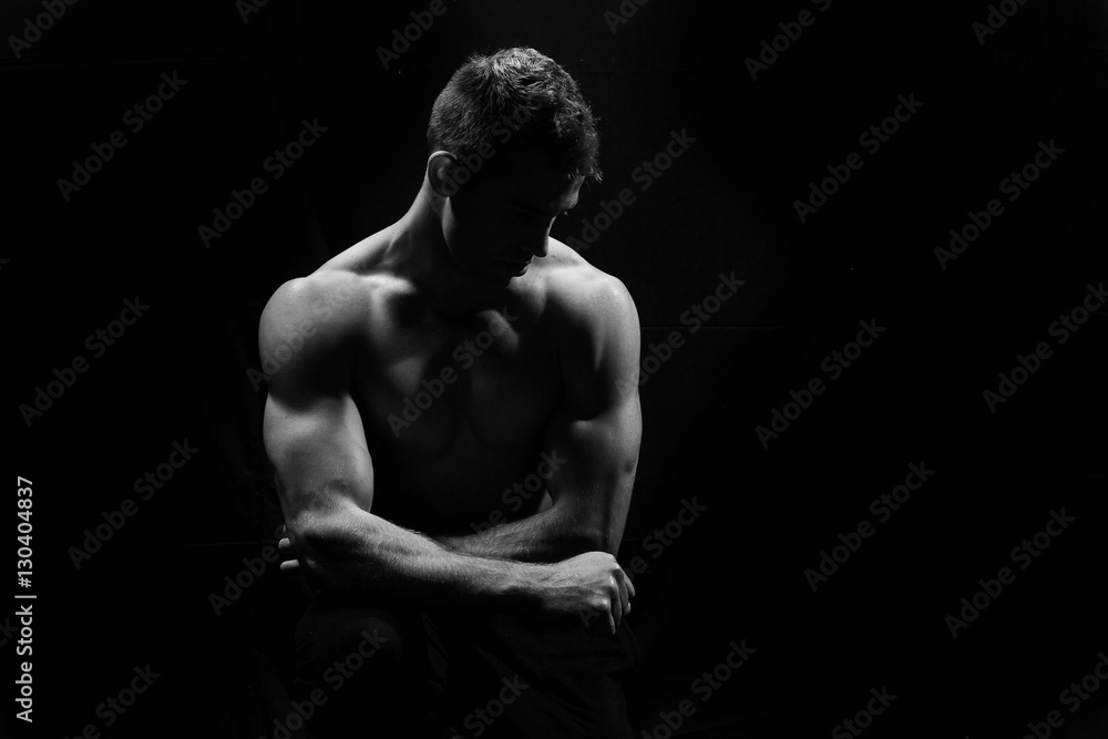 Male fitness model showing muscles in studio with a black backgr Male fitness model showing muscles in studio with a black backgr