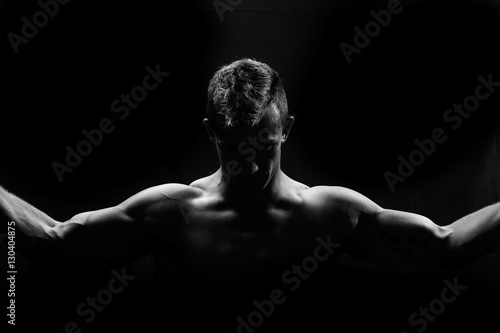 Male fitness model showing muscles in studio with a black backgr © Dewald