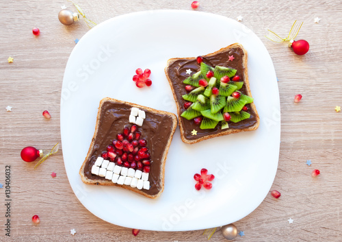 Chocolate sandwich with marshmallow and pomegranate Santa Claus hat and kiwi Christmas tree - creative idea for kids breakfast, dessert or holiday meal, top view flat lay, blank space for text