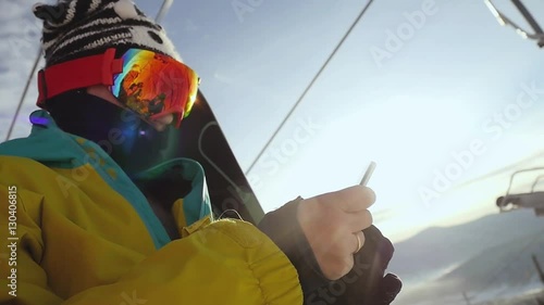 Skier in glasses with mobile phone on chair lift through the sunshine in slow motion. 1920x1080