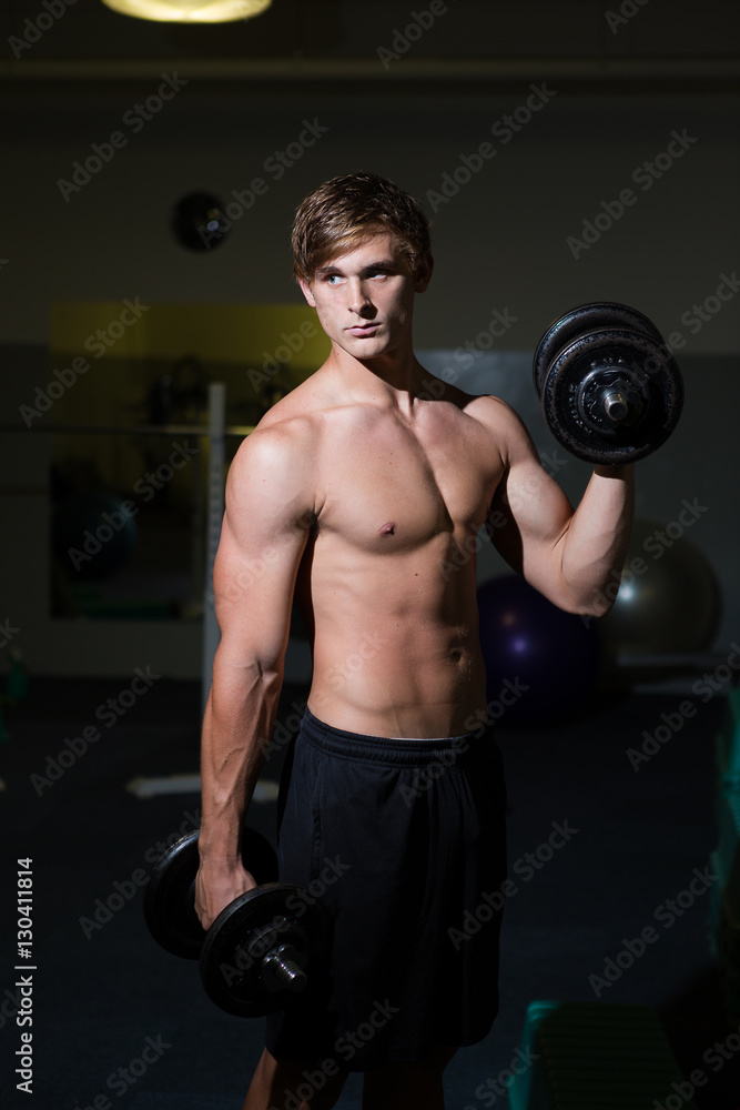 A Good looking male model flexing his muscles in a gym using wei