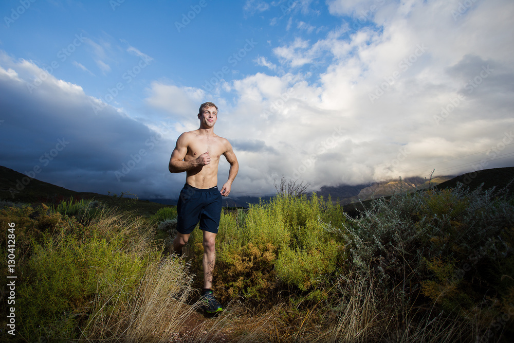 Male fitness model running allong a trail in the field, bare che