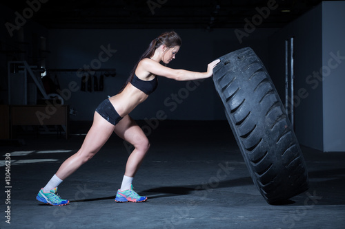 Female fitness model flipping a tyre in a gym © Dewald