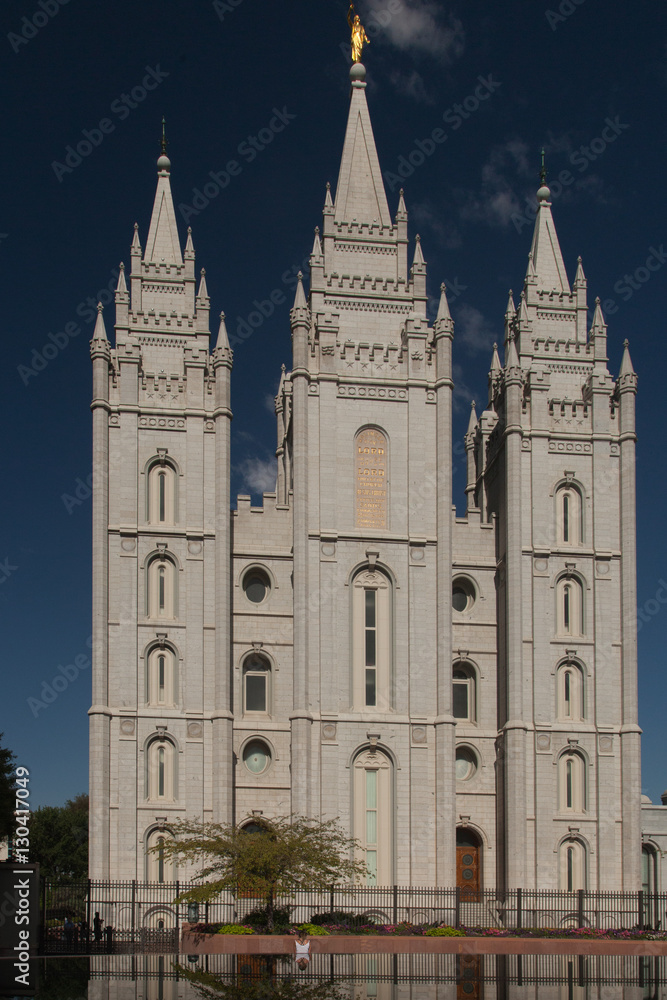Girl sitting in front of Mormon Temple is reflected in pond in foreground of photo.