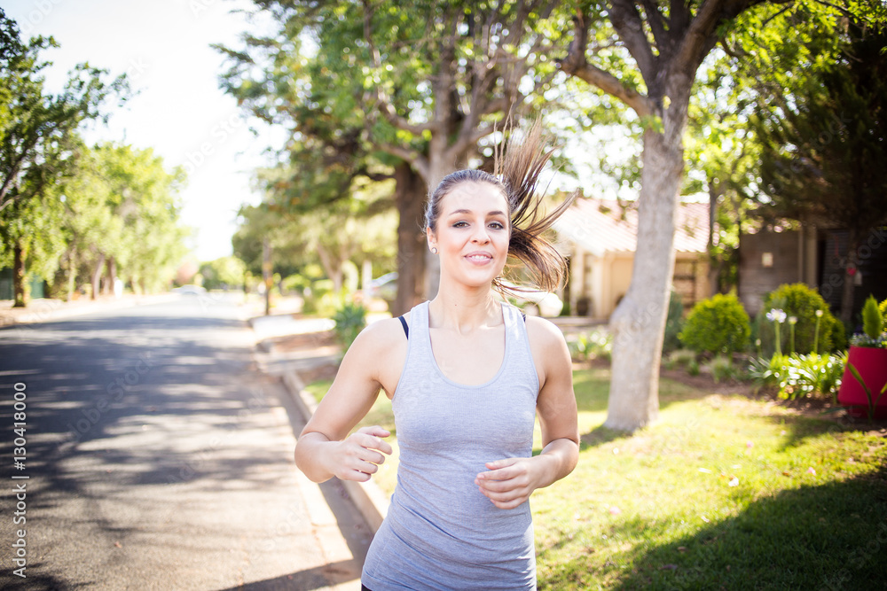 Female fitness model running and jumping in a street in a suburban area while training Female fitness model running and jumping in a street in a suburban area while training