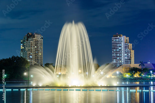 An ornamental fountain arches gracefully into the air at night above the lake at Queen Sirikit National Convention Center in Downtown Bangkok, Thailand. 