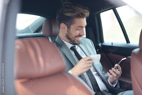 Happy young businessman using mobile phone in back seat of car © ASDF