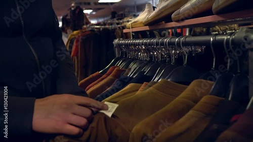 Closeup. Young man shopping, choose clothes in mall. Man want to buy a jacket