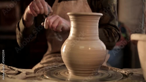 close up of potter's hands designing pattern on traditional pottery by chisel with blurry other equipments on desk, clay, photo