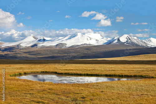 Landscape steppe shore lake with dry yellow grass and high mountain range with snow glaciers ice, Ukok Plateau, Altai, Siberia, Russia