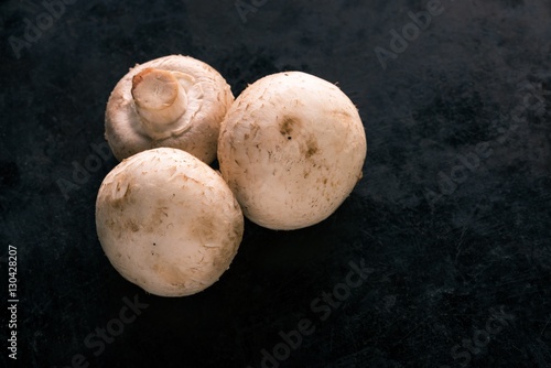 Three champignon mushrooms on dark board